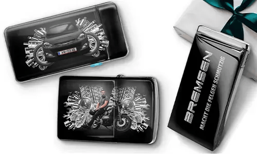 Elegante Geschenkboxen mit einem blauen Auto und einem Biker, umgeben von metallischen Zahnrädern. Eine Box trägt den Text „BREMSEN Macht Die Regeln Schmutzig“, was einen dynamischen, kantigen Ton hinzufügt.