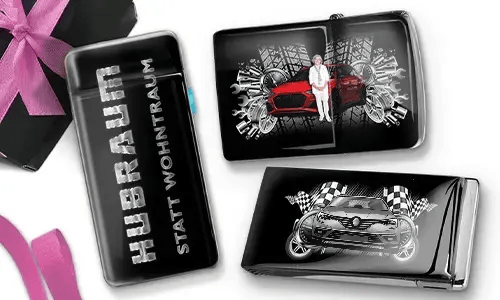Drei Zigarettenetuis in Schwarz und Silber mit dynamischen Auto-Grafiken. Eines trägt die Aufschrift „Hubraum statt Wohntraum“, während die anderen Rennmotive zeigen.
