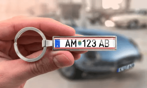 Custom license plate keychain held in hand with car in background