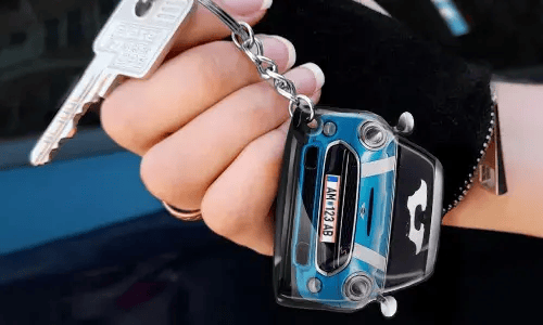 Käsi pitää avaimenperää, joka on muotoiltu siniseksi autoksi yksityiskohtaisella etuosalla