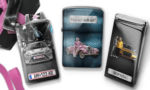 Drei Metallfeuerzeuge mit personalisierten Designs. Das linke Feuerzeug zeigt eine Stadtsilhouette und ein Paar neben einem Auto mit der Aufschrift „BESTE OMA DER WELT“. Das mittlere Feuerzeug stellt ein rosafarbenes Oldtimer-Auto dar, darüber steht „HAB DICH LIEB OMA“. Das rechte Feuerzeug zeigt ein blaues Auto und ein Kennzeichen. Rosafarbene Schleifen verleihen dem Ganzen einen Geschenkcharakter.