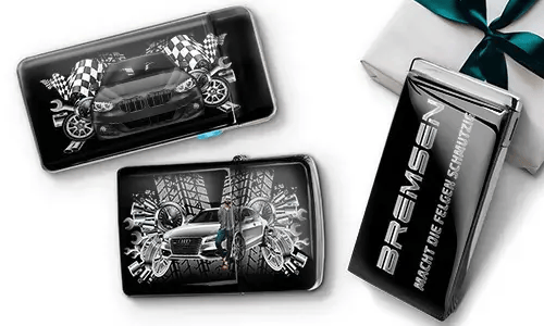 Car-themed wallets featuring sleek cars, checkered flags, and tire patterns on a black background. Beside them, a black gift box with silver text.