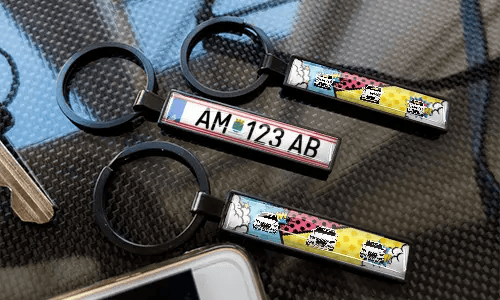 Porte-clés avec plaque d’immatriculation style bande dessinée, exposés sur une surface à texture carbone avec des designs de voitures colorés