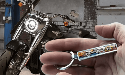 Porte-clés style bande dessinée avec plaque d’immatriculation, tenu dans une main avec une moto en arrière-plan