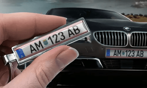 Nøkkelring i tegneseriestil med bilskilt, holdt i hånden foran en bil med matchende skilter