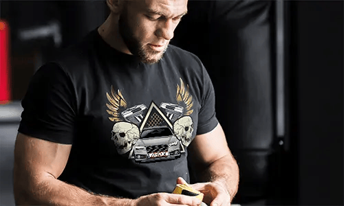 Black T-shirt with graphic of car, skulls, pistols, golden wings, and starry triangle background