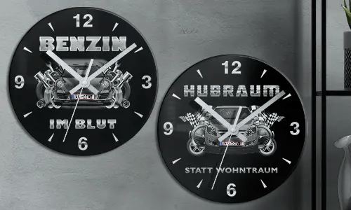 Zwei schwarze Wanduhren mit Autoillustrationen und deutschem Text: BENZIN IM BLUT und HUBRAUM STATT WOHNTRAUM